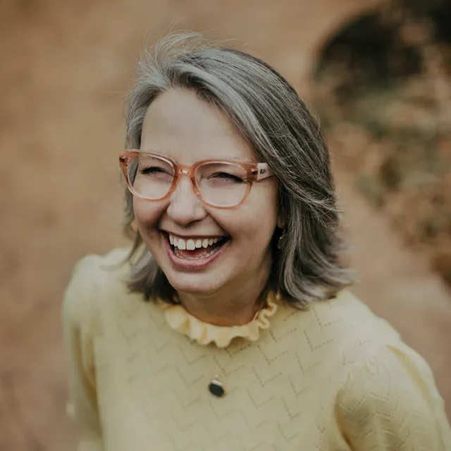 Renée Nicholson, an academic with square glasses and shoulder-length gray hair, shown laughing. 