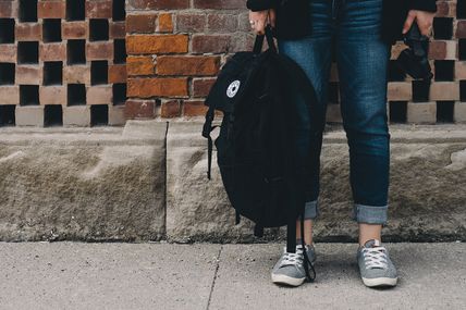 A student holding a backpack by her legs.